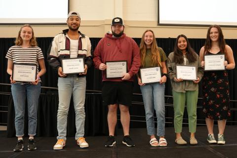 Six MUB employees stand on stage holding their award certificates.